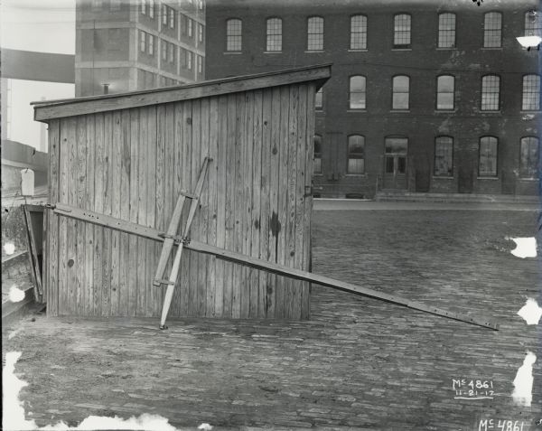 A pole and evener for horse-drawn farm machinery leaning up against a shed. The shed is in a factory yard at McCormick Works.