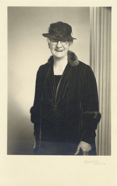 Portrait of Anita McCormick Blaine (1866-1954) later in life. She is wearing a black velvet dress, fur-trimmed coat, a small hat and round eyeglasses. She is laughing.