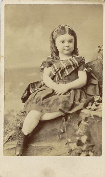 Portrait of Anita McCormick Blaine (1866-1954) as a young girl. She wears a striped sash over an embroidered dress, and a ribbon in her hair.