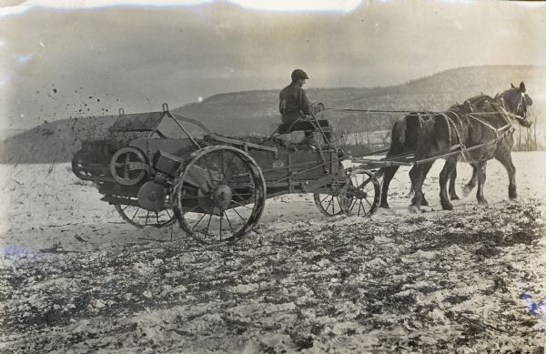 A young man driving a two-horse manure spreader in a snowy field.