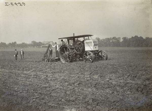 The 25 H.P. Titan tractor with 4-bottom Oliver Plow attachment on the farm of the Siegal Brothers. Charles Stiegal is operating the plow while four other men stand on or near the tractor.
