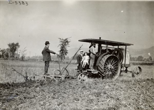 An International 20 H.P. Type B Tractor owned by J.S. Curtis, but operated by G.W. Crosby. According to the original caption, Crosby operated the outfit without assistance, plowing about 10 acres per day and sometimes as much as 17 acres in one and a half days. A young girl is sitting on a man's lap, who is sitting behind the man driving the tractor, while another man is standing on the plow.