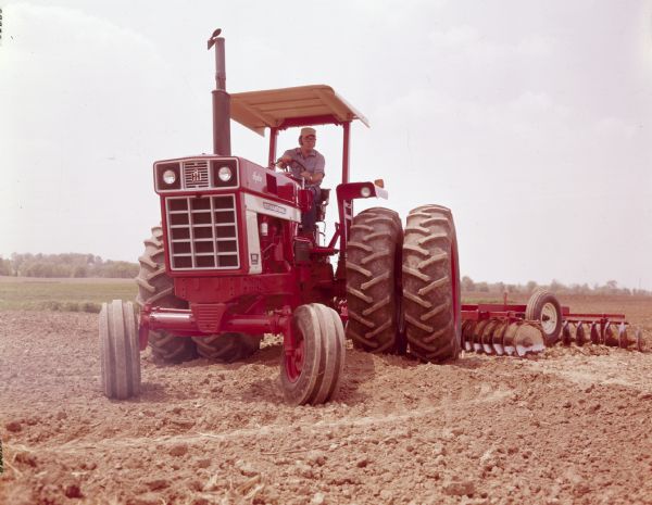 Color photograph of a man operating an International 1066 Hydro Tractor with a 370 Disc, 13 foot and 10 inch Disc Harrow atttachment.