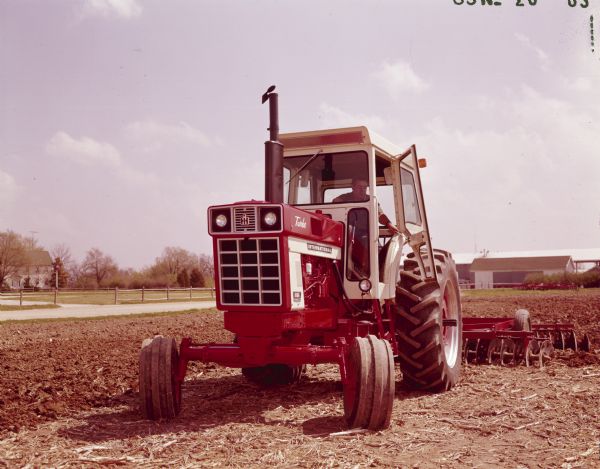 Color photograph of a man operating an International Turbo 1066 tractor with cab and Disc Harrow attachment.