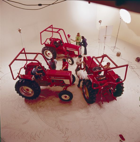 Elevated view of three International Harvester tractors in a photo studio. Groups of three people surround each tractor talking; the lights used for the photographs are in the background.
