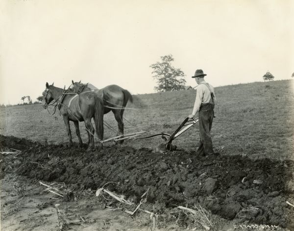 A farmer using a Chattanooga walking plow drawn by two horses.