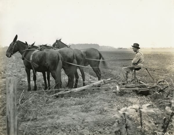 A farmer is sitting on the seat of a Chattanooga plow pulled by four horses.