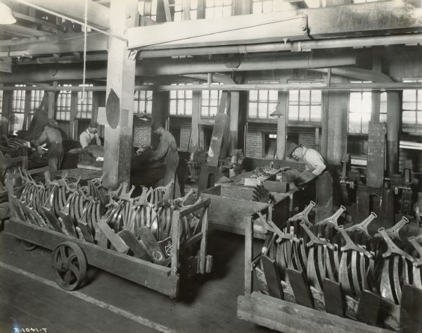 Factory workers working at tables, and long wheeled carts full of implement parts at the Chattanooga Plow Works.