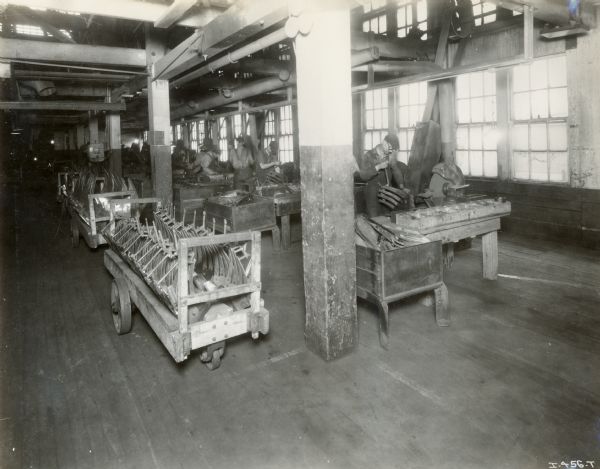 Factory workers working at tables, and long wheeled carts full of implement parts at the Chattanooga Plow Works.