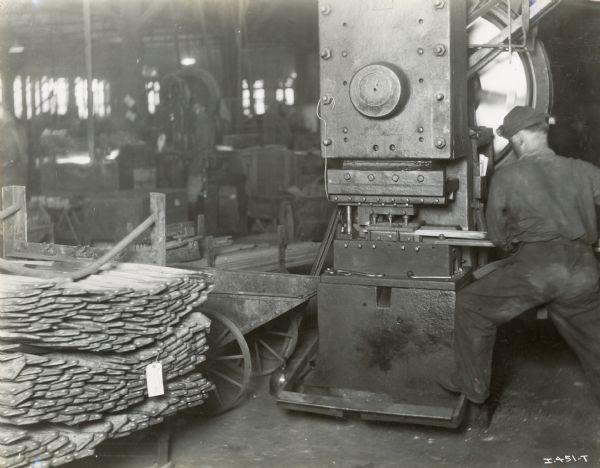 A man inserts a board into a machine (possibly a drill press) at the Chattanooga Plow Works.
