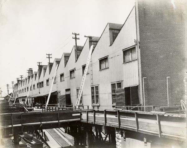 Exterior view of a loading (?) area of the Chattanooga Plow Works, with multiple ladders leaning against the building. There are wagons on the ground below the walkways and ramps.