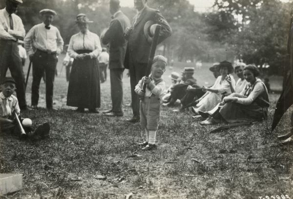 A young boy holding a baseball bat at a Harvester Club picnic.