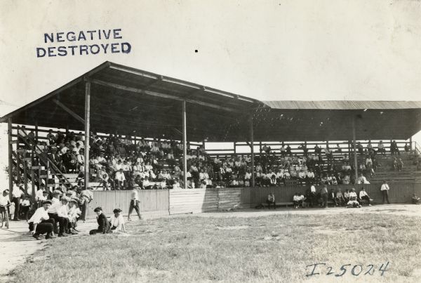Spectators in bleachers watch a baseball game as part of the Milwaukee and West Pullman Works Fire Department Exhibition at West Pullman Park.