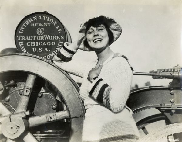 A woman poses with her elbow leaning against an International Harvester tractor, possibly a Mogul 8-16.