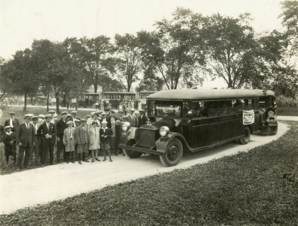 A crowd of International Harvester employees gathers near buses lined up to transport them to or from the Harvester Club picnic at the IH experimental farm.