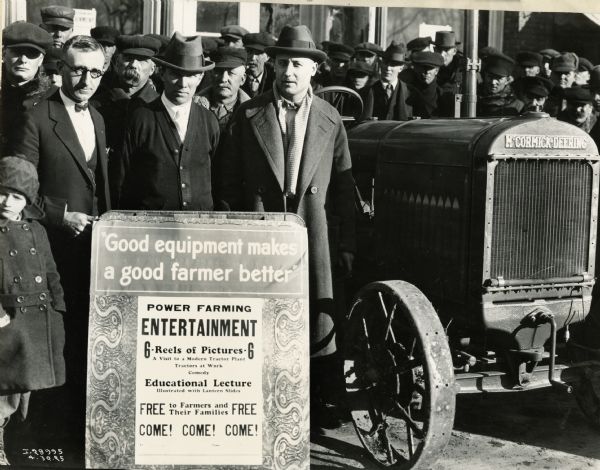 A group gathers near a McCormick-Deering tractor and a sign advertising a power-farming lecture.