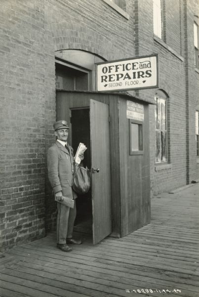 A mail carrier pauses outside the back door to an International truck dealership or branch house. A sign above the door advertises "repairs" on the second floor.