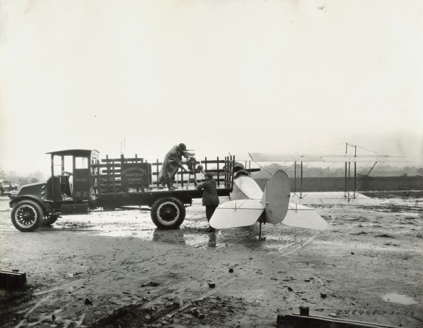 Two men ready a cream separator from Milwaukee Works to be transported to Hinsdale by airplane. One man is standing in the bed of a truck.