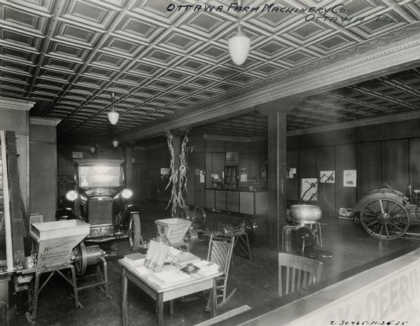 A man sits behind a desk in the showroom of the Ottawa Farm Machinery Company, an International Harvester dealership. A truck, tractor, feed grinder and cream separator are on display.