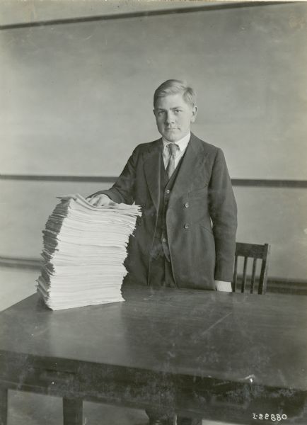 An office worker, most likely an employee of International Harvester, stands behind a table with his hand held on top of a stack of papers.