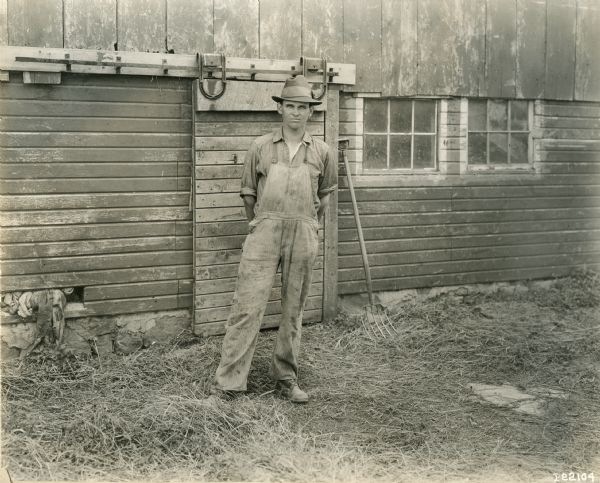 A farmer, standing near a barn and pitchfork for a portrait.