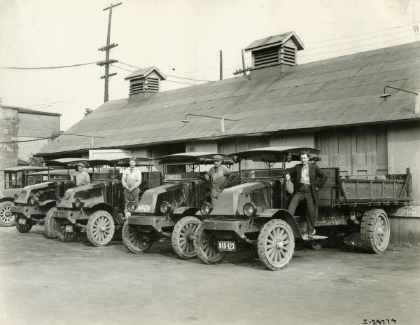 Four men standing on International Model "L-101" trucks equipped with 4 yard bodies and underbody hoists.  The trucks carried 16 loads a day of 7 tons per load. The original photograph is labeled "Scott Bros."