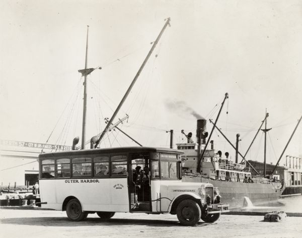 International "outer harbor" bus parked near a large boat and several harbor buildings. The bus was built on an International model 52 or model 53 chassis.