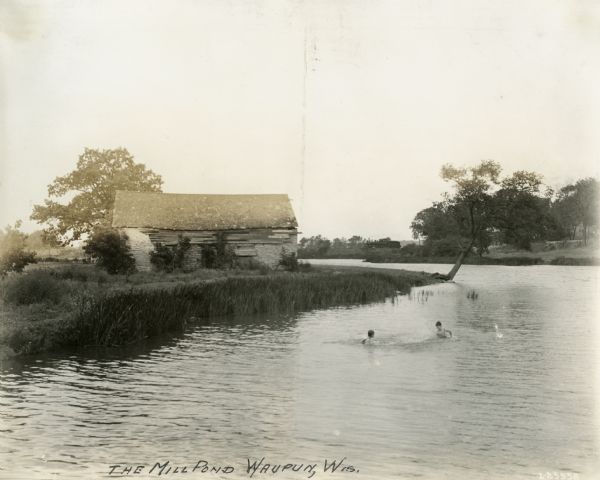 Two young boys swim in a mill pond beside a dilapidated building.