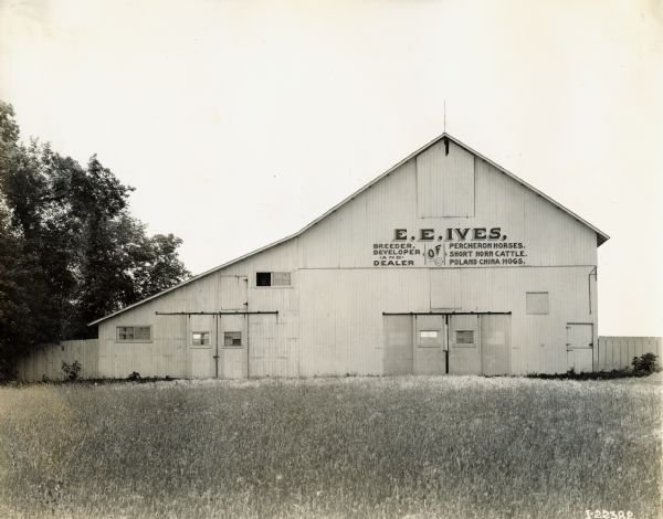 Exterior view of a building on the E.E. Ives farm. A sign on the building reads: "E.E. Ives, Breeder, Developer, and Dealer of Percheron Horses, Short Horn Cattle, Poland China Hogs."