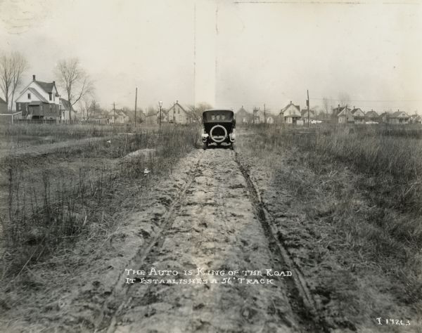 Rear view of an automobile leaving a 56 inch track on a dirt road. The photo and original caption were probably used to advertise farm wagons with a similar track width.