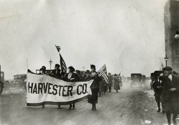 Women, possibly International Harvester employees, carrying American flags and a company banner in a parade. The parade may be on Michigan Avenue in Chicago, outside the company's headquarters building.