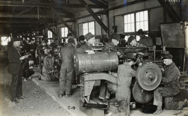 Groups of students work on tractors, including a Titan 10-20, at the Kansas State Agricultural College. Two men (professors?) watch and take notes while students work on machines.
