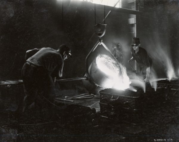 Two factory workers pour molten metal into diesel engine crankcase forms at the Milwaukee Works foundry. Photograph taken by Don Jones.