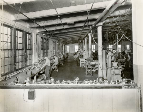 Factory workers at a long bench and at various work stations in a large room at Milwaukee Works.