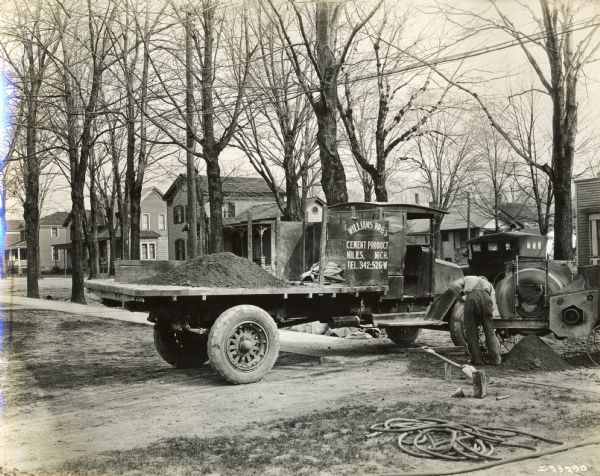 A man working on a residential street with a shovel and an International Model G-61 truck. The truck was operated by the Williams Brother's Concrete and Cement Contractor Company.