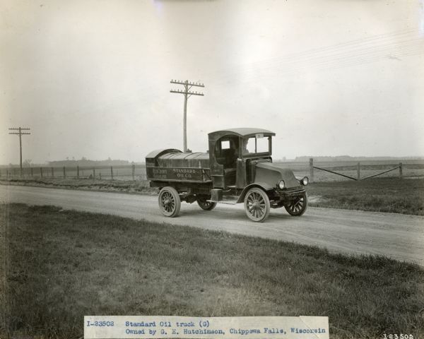 A man drives an International Model G-61 truck on a rural road with power lines. The truck was operated by G.E. Hutchinson's Standard Oil Company business.