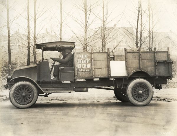 Two men sit in the cab of an International Model G-61 truck operated by the Maine Creamery Ice Cream Company. A sign on the side of the truck reads: "The National Dessert."