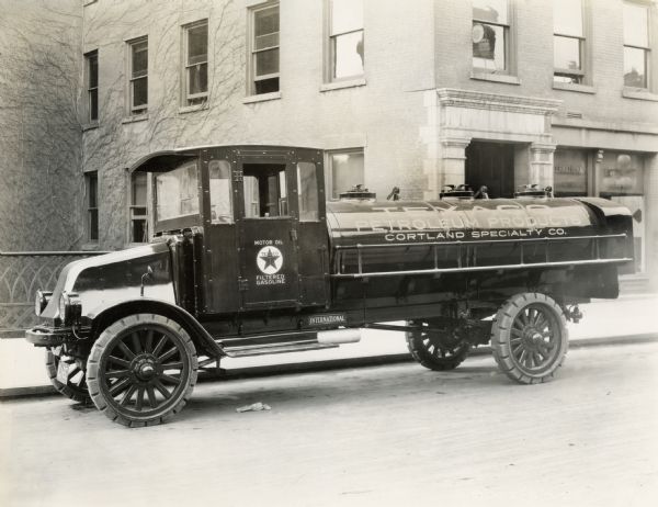 An International Model G-61 tanker truck parked on a city street. The writing on the truck reads: "Texaco Motor Oil, Filtered Gasoline; Texaco Petroleum Products Cortland Specialty Co."