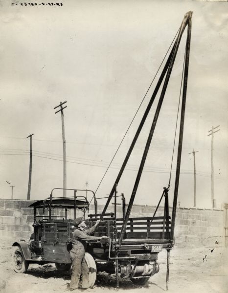 An employee operates an International Model G or 61 truck with Mead-Morrison under-slung winch and derrier equipment for the Lowell Electric Lighting Company and New England Telephone and Telegraph Company.