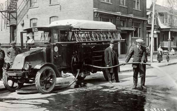Firefighters handle a fire hose connected to an International Model 61 1923 fire truck operated by the "Canadian Fire Department."