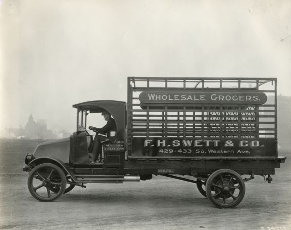 A man drives an International Model G or 61 truck with a large metal bed frame for Wholesale Grocers of F.H. Swett and Company.