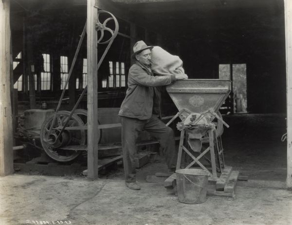 A man pours a bag of feed into a feed grinder powered by a 6 h.p. engine.