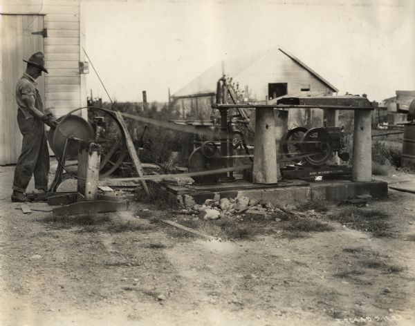 A man uses a 1 1/2 H.P. McCormick-Deering engine to pump water and run a grindstone.