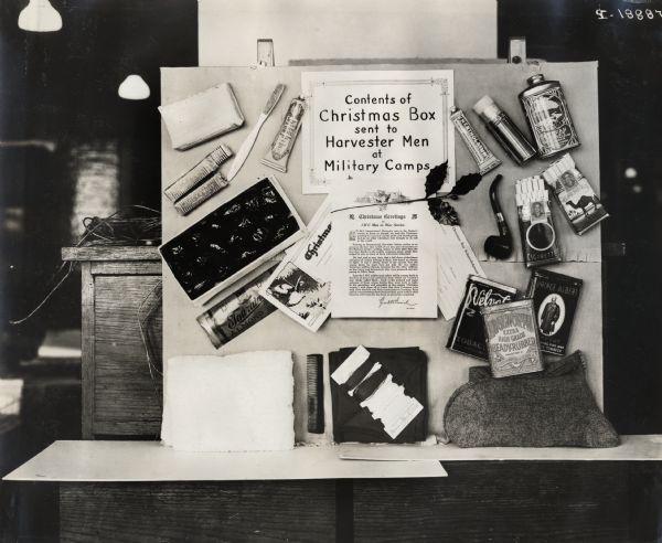 Display board of samples of items sent to "Harvester men at military camps" for Christmas. The display includes a toothbrush and toothpaste, a candy bar, thread, a comb, a pipe and tobacco, cigarettes, socks, and talcum powder.