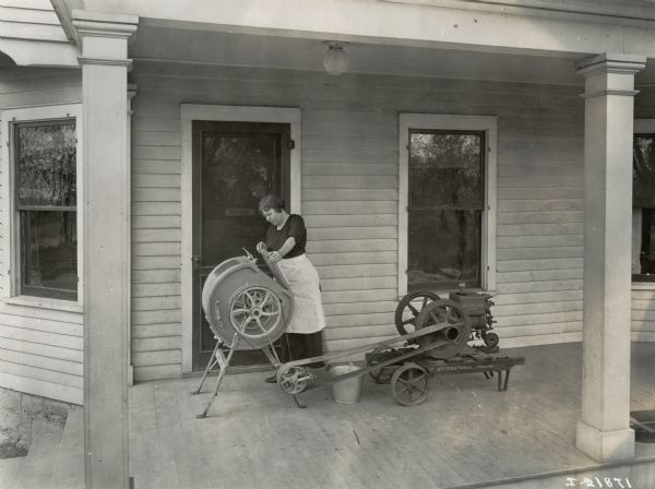 A woman operates a home creamery powered by an International Harvester engine on a porch.