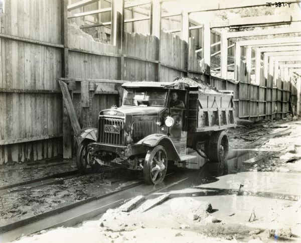 A man drives an International dump truck through a construction site.