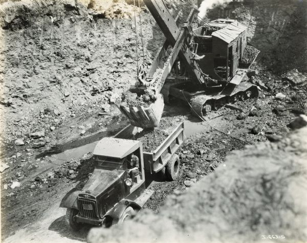 Elevated view of a steam shovel filling the back of an International truck with dirt at an airport construction site.