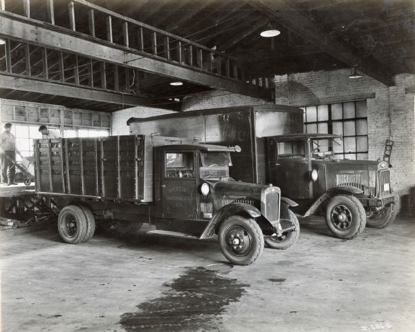 Two International trucks parked inside a loading dock are being filled with boxes by two men.