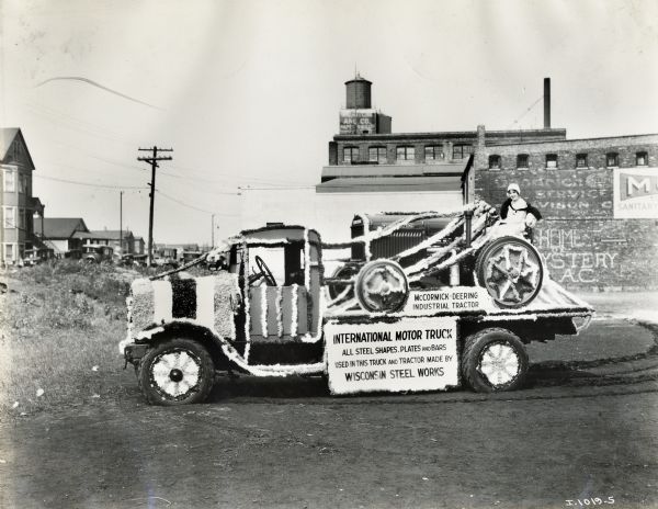 International motor truck, possibly decorated for a parade. A woman rides on a McCormick-Deering tractor placed on the truck's bed. The sign on the truck reads: "International Motor Truck; All steel shapes, plates, and bars used in this truck and tractor made by Wisconsin Steel Works."