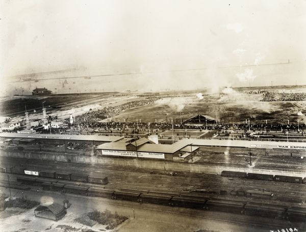 Elevated view of the U.S. Government War Exposition at Grant Park taken from a window the International Harvester building on Michigan Avenue. A large sign on one of the main buildings reads: "Three Miles of Trenches! Actual Battle! Real Fighting! 25 Carloads of War Trophies!"